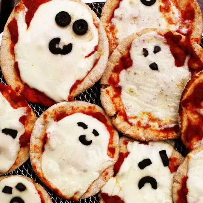 Picture of mini round shaped pizza, but the mozzarella cheese on the top is melted in a shape of a ghost.